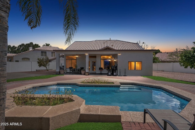 back of house at dusk featuring a patio, a fenced backyard, a fenced in pool, and stucco siding