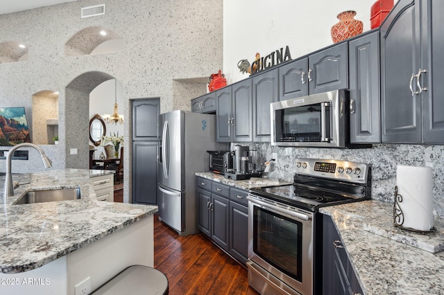 kitchen featuring light stone counters, stainless steel appliances, a sink, visible vents, and dark wood-style floors