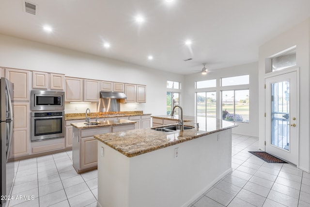 kitchen with light stone countertops, stainless steel appliances, ceiling fan, a kitchen island with sink, and sink