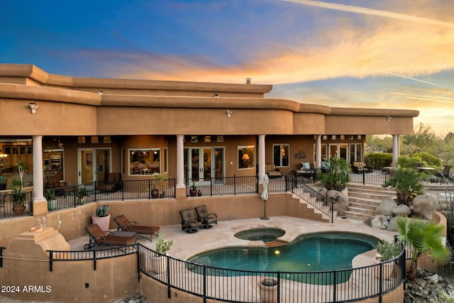 back house at dusk featuring a swimming pool with hot tub and a patio