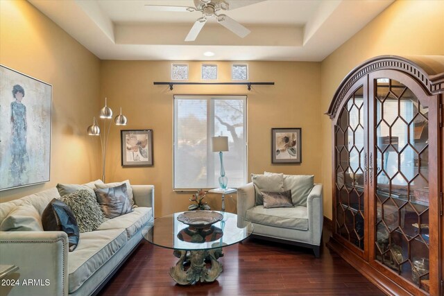 living room featuring a raised ceiling, ceiling fan, and dark hardwood / wood-style floors