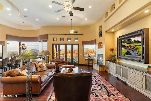 living room with ceiling fan with notable chandelier, dark wood-type flooring, a high ceiling, and french doors