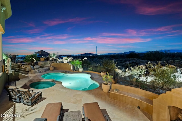 pool at dusk with an in ground hot tub and a patio area