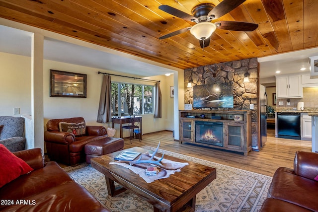 living room with ceiling fan, a stone fireplace, light hardwood / wood-style floors, and wooden ceiling