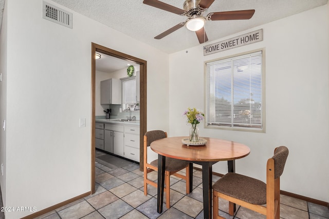 tiled dining room with a textured ceiling, sink, and ceiling fan