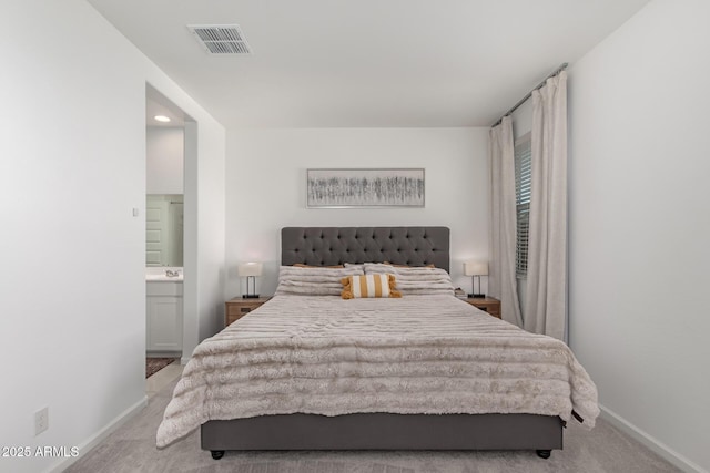 bedroom with ensuite bathroom and light colored carpet