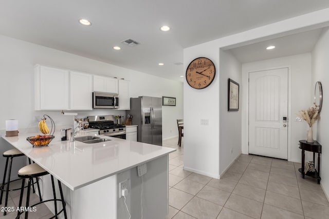 kitchen with kitchen peninsula, appliances with stainless steel finishes, a breakfast bar, and white cabinets