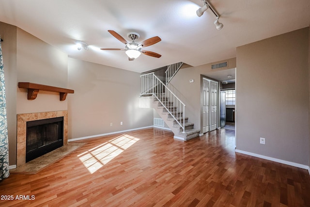 unfurnished living room featuring a tiled fireplace, wood-type flooring, rail lighting, and ceiling fan