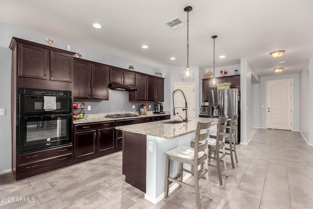 kitchen with visible vents, stainless steel appliances, dark brown cabinets, a kitchen bar, and a sink