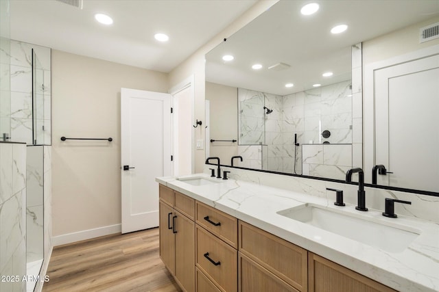 bathroom with wood finished floors, recessed lighting, a marble finish shower, and a sink