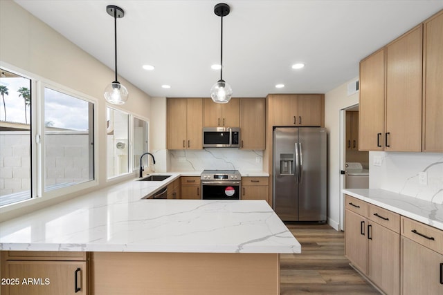 kitchen featuring tasteful backsplash, a peninsula, stainless steel appliances, washer / clothes dryer, and a sink