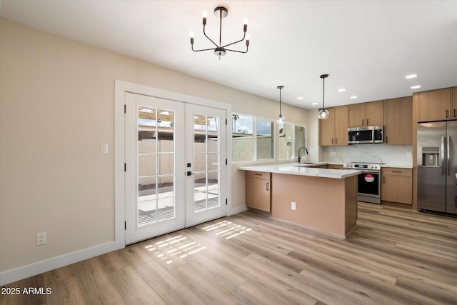 kitchen featuring a sink, french doors, light wood-style floors, appliances with stainless steel finishes, and a peninsula