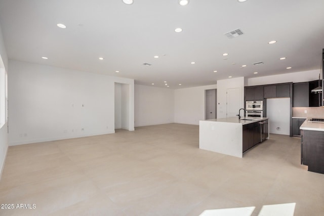 kitchen with visible vents, an island with sink, light countertops, dark brown cabinets, and recessed lighting