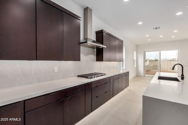 kitchen with stainless steel gas cooktop, a sink, visible vents, backsplash, and wall chimney exhaust hood