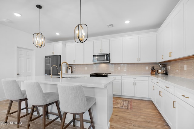 kitchen featuring sink, an island with sink, fridge, and white cabinetry