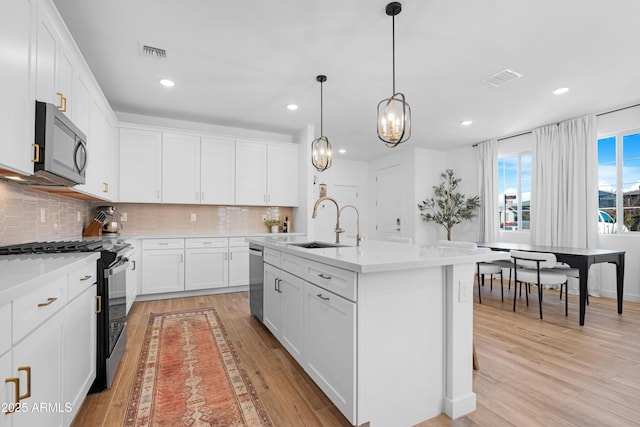 kitchen with hanging light fixtures, an island with sink, white cabinetry, appliances with stainless steel finishes, and sink