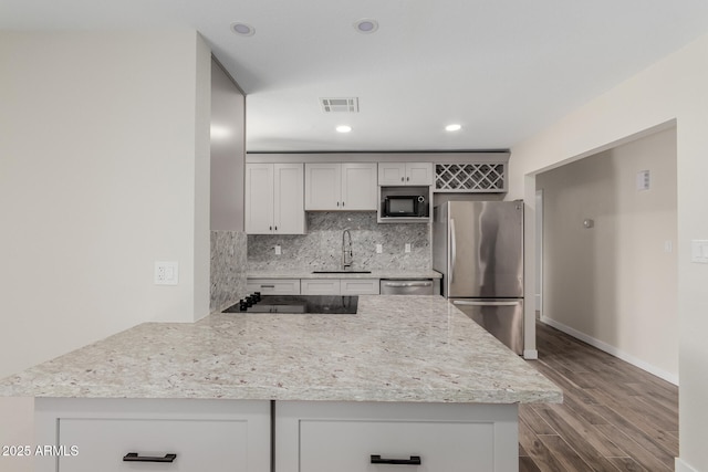 kitchen featuring dark wood-type flooring, a sink, visible vents, black appliances, and tasteful backsplash