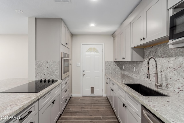 kitchen featuring wood finish floors, stainless steel appliances, tasteful backsplash, a sink, and light stone countertops