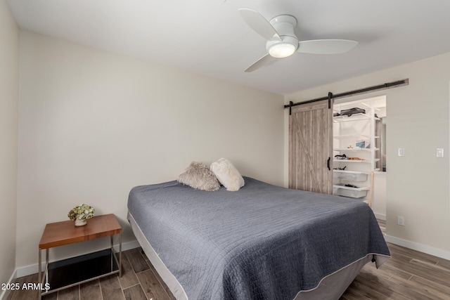 bedroom featuring a ceiling fan, a barn door, baseboards, and wood finished floors