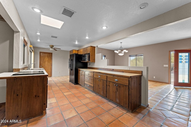 kitchen with kitchen peninsula, a skylight, black fridge with ice dispenser, and pendant lighting