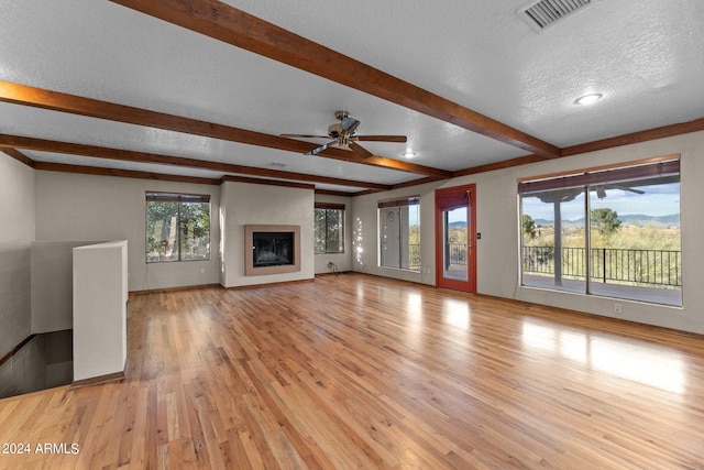 unfurnished living room featuring beam ceiling, ceiling fan, light hardwood / wood-style floors, and a textured ceiling