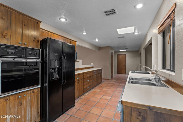 kitchen with black appliances, sink, a skylight, a textured ceiling, and light tile patterned flooring