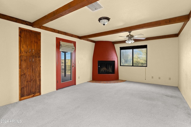 unfurnished living room with carpet floors, ceiling fan, a fireplace, and beamed ceiling