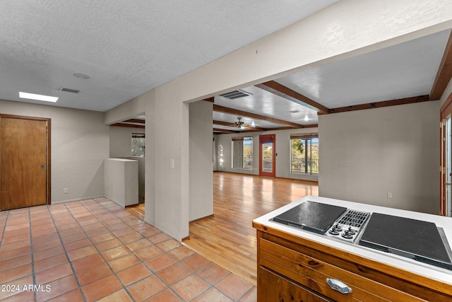 kitchen with beamed ceiling, ceiling fan, a textured ceiling, and light hardwood / wood-style flooring