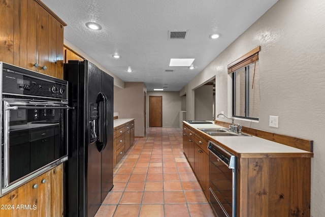 kitchen with black appliances, sink, a skylight, light tile patterned floors, and a textured ceiling