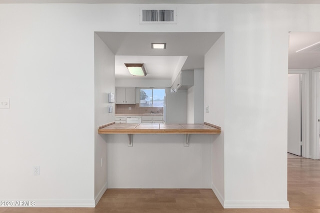 kitchen with a kitchen bar, visible vents, white dishwasher, light wood finished floors, and tile counters