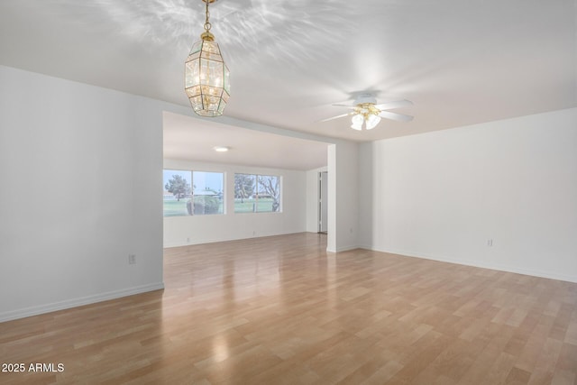 spare room with light wood-style floors, ceiling fan with notable chandelier, and baseboards