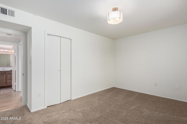 unfurnished bedroom featuring visible vents, baseboards, a closet, and light carpet