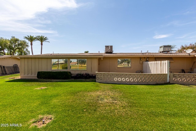 rear view of property with central air condition unit, fence, and a lawn