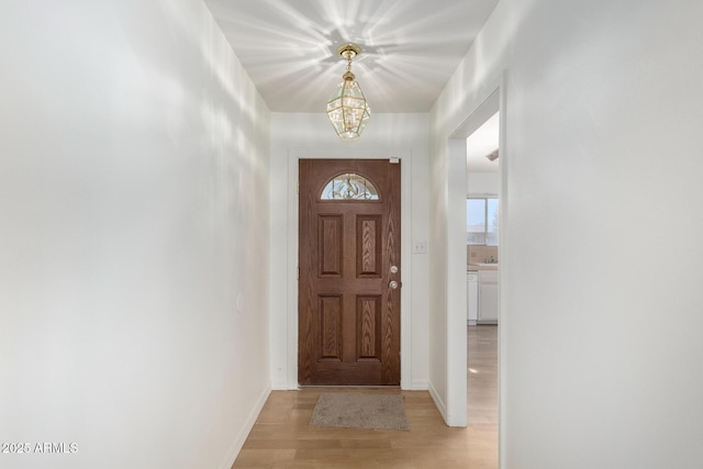 foyer entrance featuring baseboards, a notable chandelier, and light wood-style floors