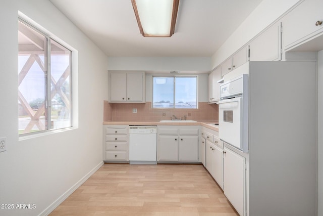 kitchen with white appliances, light wood-style flooring, white cabinets, light countertops, and decorative backsplash