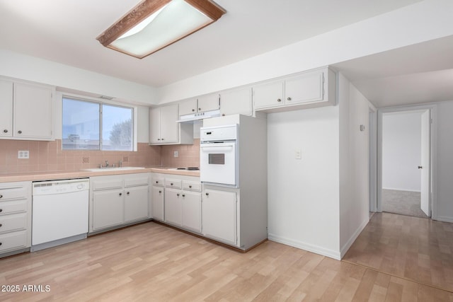 kitchen featuring light countertops, tasteful backsplash, a sink, and white appliances