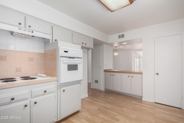 kitchen featuring tasteful backsplash, white appliances, under cabinet range hood, light wood finished floors, and white cabinetry