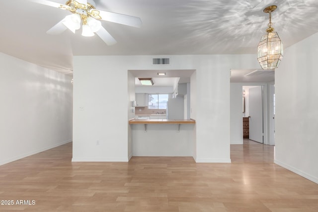 unfurnished living room with baseboards, light wood finished floors, ceiling fan, and visible vents
