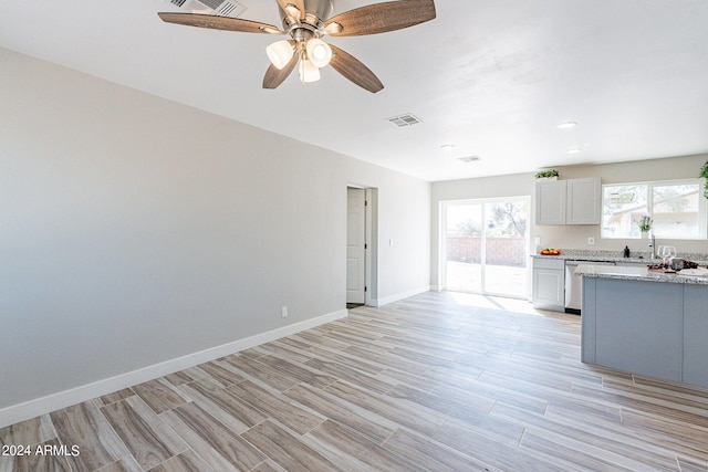 unfurnished living room featuring baseboards, visible vents, a ceiling fan, light wood-type flooring, and a sink