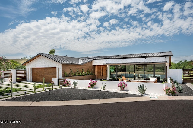 view of front of home with metal roof, a garage, fence, driveway, and a standing seam roof