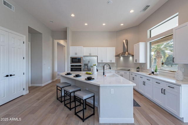 kitchen featuring white cabinetry, wall chimney range hood, a kitchen island with sink, and appliances with stainless steel finishes