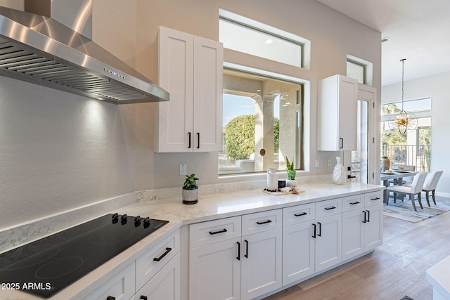 kitchen featuring black electric stovetop, white cabinets, wall chimney range hood, and light stone counters