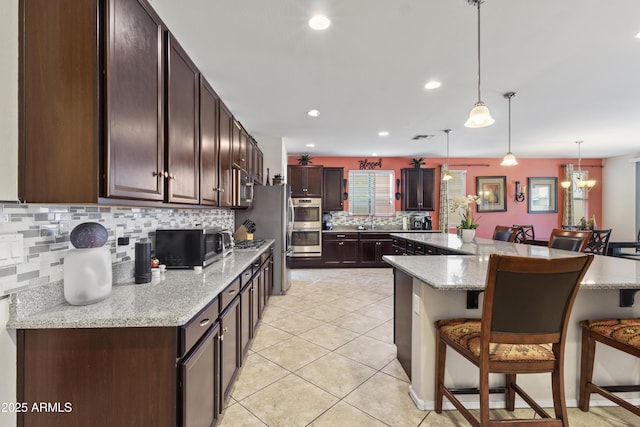 676 N 156th Ln, Goodyear, AZ 85338 - kitchen featuring light tile patterned floors, stainless steel appliances, a kitchen breakfast bar, hanging light fixtures, and light stone countertops
