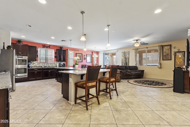 676 N 156th Ln, Goodyear, AZ 85338 - kitchen with a breakfast bar area, appliances with stainless steel finishes, open floor plan, light stone counters, and hanging light fixtures