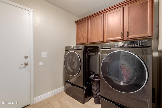 clothes washing area featuring cabinets, separate washer and dryer, and light wood-type flooring