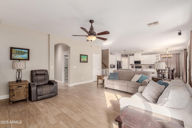 living room featuring ceiling fan with notable chandelier and light wood-type flooring