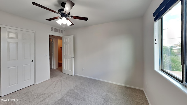 unfurnished bedroom featuring multiple windows, a closet, light colored carpet, and ceiling fan