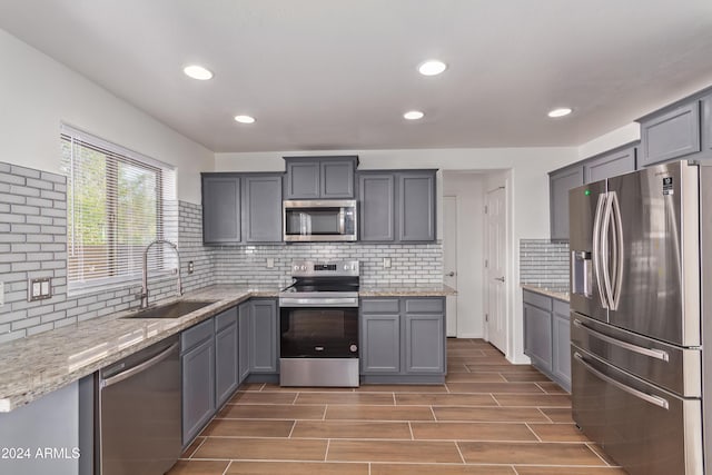 kitchen with appliances with stainless steel finishes, tasteful backsplash, sink, gray cabinets, and dark hardwood / wood-style floors