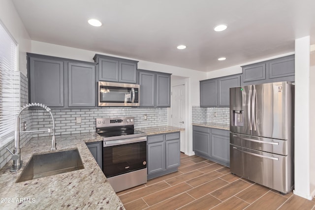 kitchen featuring light stone countertops, sink, stainless steel appliances, dark hardwood / wood-style floors, and gray cabinets