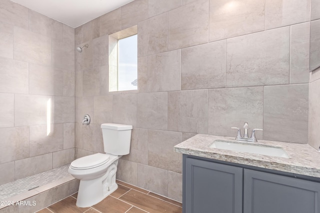 bathroom with a shower, vanity, toilet, and tile walls